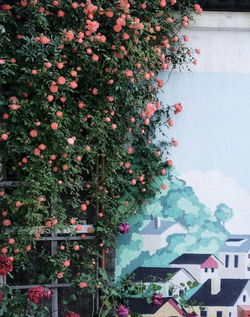 Uma parede com um mural de flores e uma casa ao fundo.