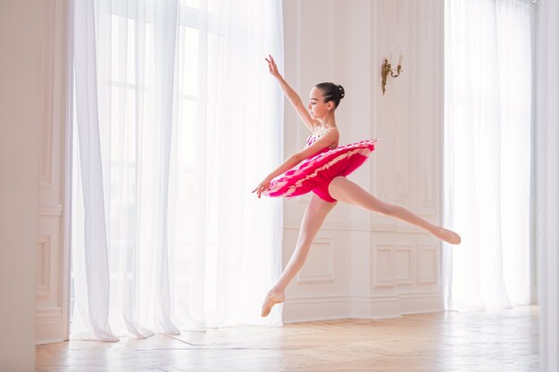 Uma pequena bailarina com um tutu rosa brilhante está dançando em um belo grande salão branco, congelou em um salto