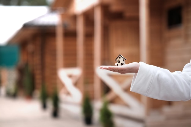 Foto uma pequena casa de madeira na mão de uma mulher contra o fundo de uma casa de madeira construída conceito de comprar uma casa ecológica feita de madeira