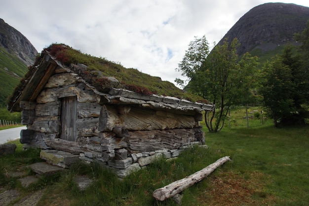 Uma pequena casa feita de troncos de grandes árvores, o telhado de terra coberto de grama, perto da montanha.