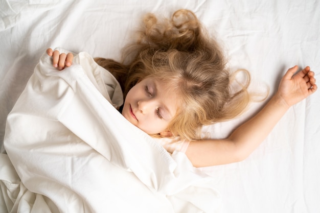 Uma pequena loira está dormindo docemente em uma cama com espaço de cueca branca para o texto sono saudável