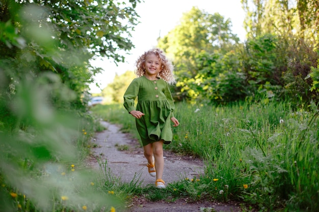 Uma pequena menina loira encaracolada corre ao longo de um caminho no parque