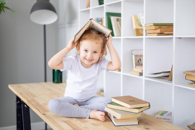 Uma pequena menina loira lê livros em uma biblioteca brilhante em educação doméstica e ciência para crianças