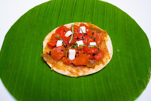 uma pequena pizza com tomates e cebolas em uma folha de banana