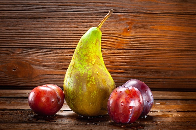 Uma pera verde-marrom molhada e ameixas maduras com gotas de água sobre fundo escuro de madeira