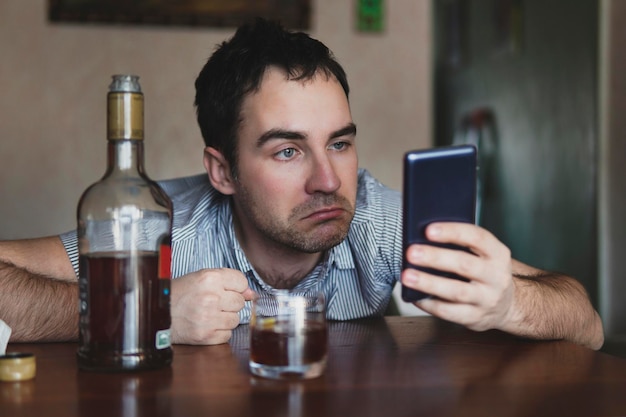 Uma pessoa bêbada está sentada à mesa em casa e lendo uma mensagem em um smartphone expressão estúpida de surpresa no rosto do bêbado um funcionário cansado fica bêbado e deprimido