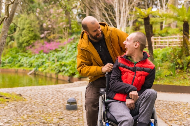 Uma pessoa com deficiência em um parque público da cidade na cadeira de rodas se divertindo andando com um amigo