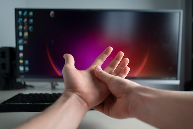 Uma pessoa com síndrome do túnel trabalhando no escritório no computador e segurando sua mão sentindo dor