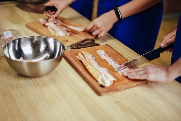 Uma pessoa cortando bacon em uma tábua