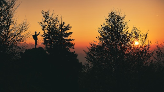 Uma pessoa em silhueta fotografa o pôr do sol na encosta