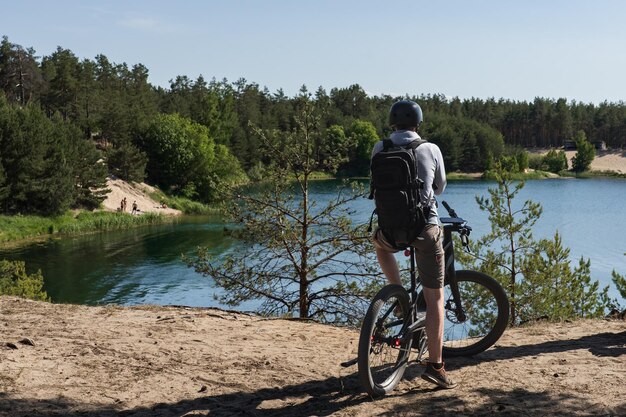 Uma pessoa em uma bicicleta olha para um lago com árvores ao fundo