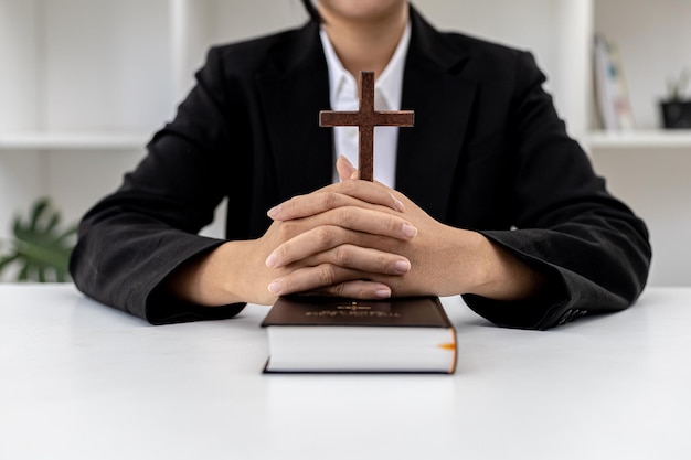 Uma pessoa entrelaçando as mãos sobre o livro da Bíblia e segurando uma cruz, ele está orando à Bíblia, ele lê e estuda a Bíblia. Conceito de Cristianismo e Estudo da Bíblia.