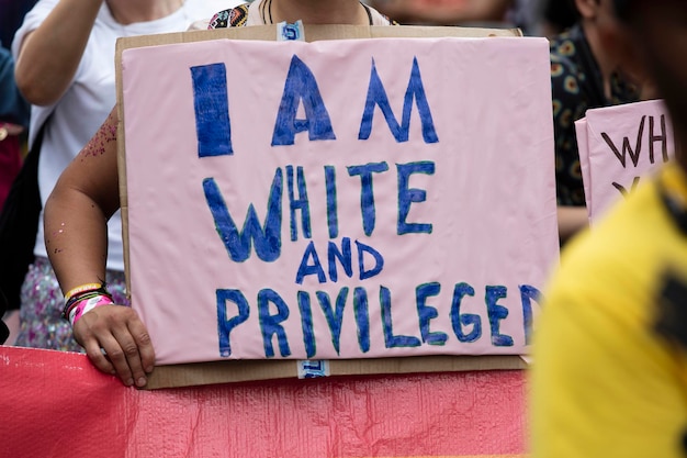 Uma pessoa segurando um banner eu sou branco e privilegiado em um evento de orgulho gay