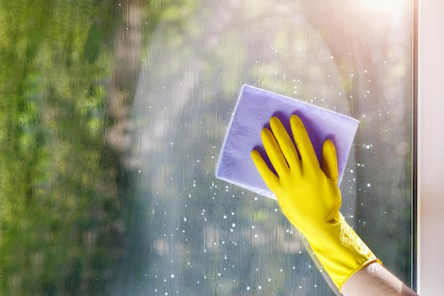 Uma pessoa usando luvas amarelas está limpando uma janela com uma esponja.