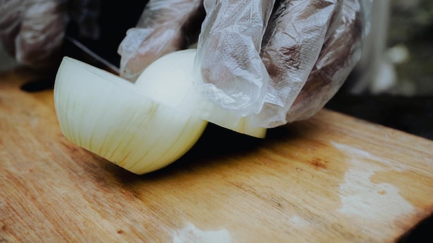 Foto uma pessoa usando uma luva de plástico está usando um pedaço de alho para cortar uma cebola.
