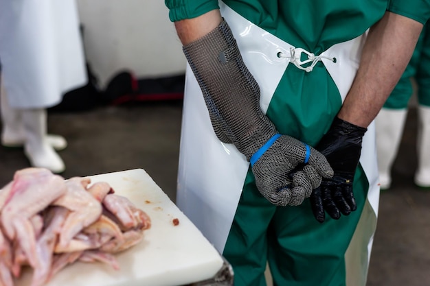 Uma pessoa vestindo um avental verde está em frente a um frango cru.