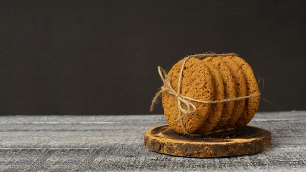 Uma pilha de biscoitos de aveia enrolados com fio de barbante repousa sobre uma tábua redonda de madeira