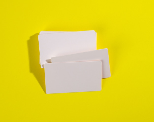 Uma pilha de cartões retangulares brancos em uma superfície amarela, marca da empresa, endereço. Vista de cima
