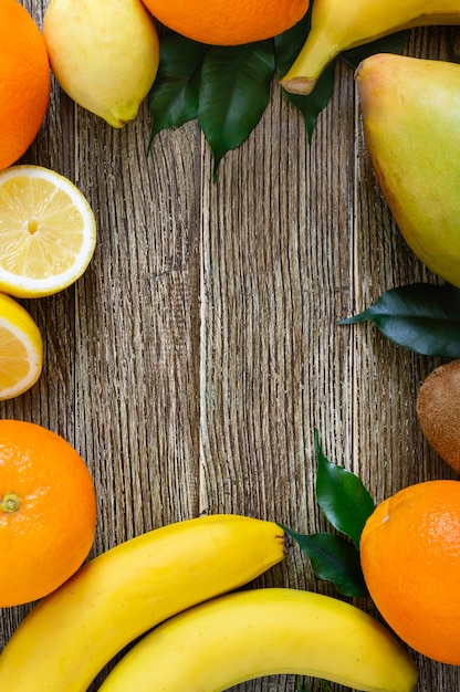 Uma pilha de frutas exóticas (bananas, laranjas, kiwi, manga, goiaba, limão) em uma mesa de madeira. espaço livre. fundo de comida.