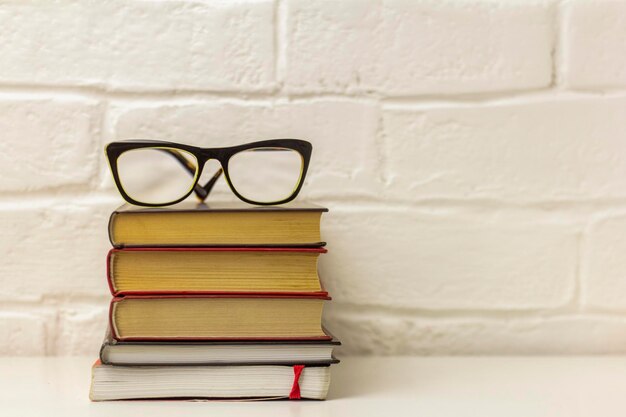 Uma pilha de livros de capa dura grossa e óculos de correção sobre a mesa. Ficção ou literatura educacional para leitura e aprendizagem.