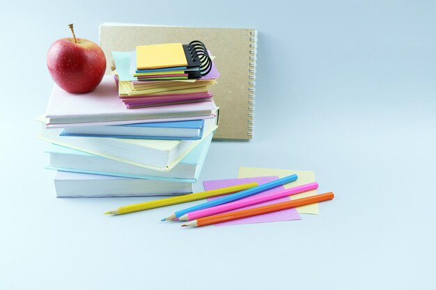 Uma pilha de livros didáticos, lápis coloridos, um caderno de esboços e uma maçã vermelha