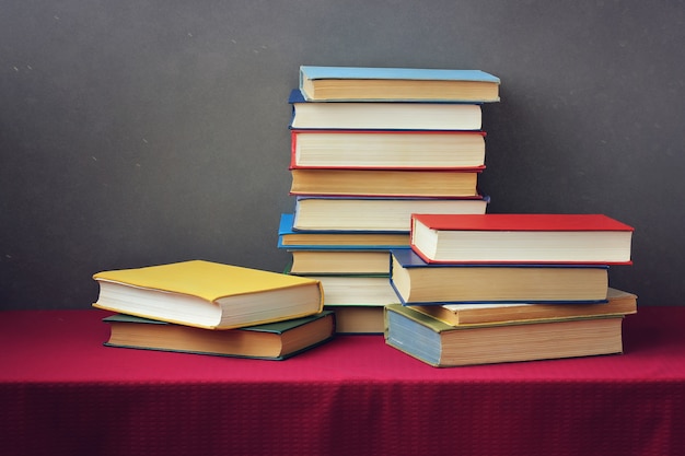 Uma pilha de livros nas capas coloridas sobre a mesa com uma toalha de mesa vermelha. Ainda vida com livros.
