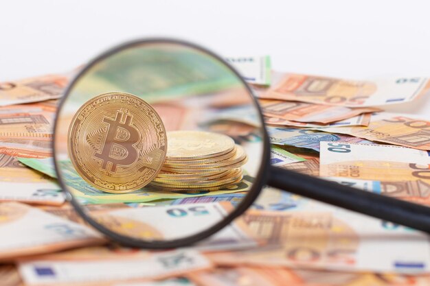 Uma pilha de moedas de bitcoin visível através de uma lupa nas notas de euro