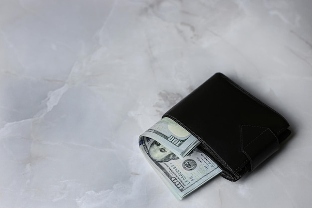 Uma pilha de notas de 100 dólares americanos dobradas em uma carteira fechada em um fundo claro