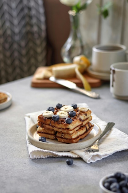 Uma pilha de panquecas com fatias de banana e mirtilos por cima.