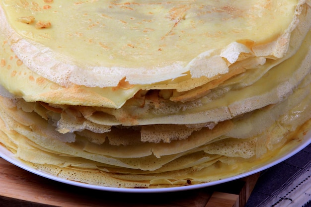 Uma pilha de panquecas finas redondas em uma placa de cozinha de madeira