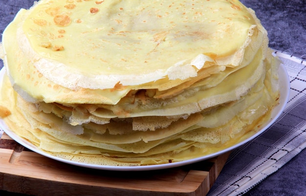 Uma pilha de panquecas finas redondas em uma placa de cozinha de madeira