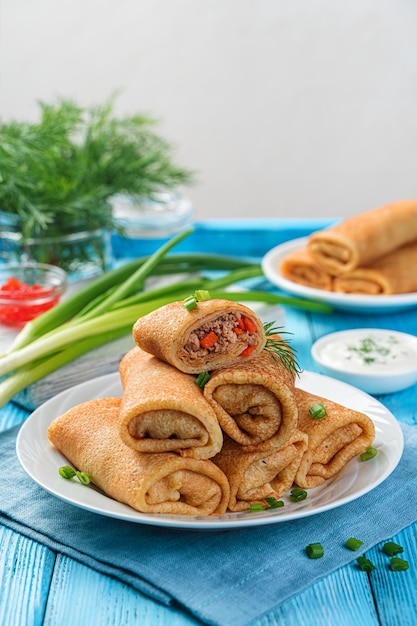 Uma pilha de panquecas recheadas fritas decoradas com endro e cebola em um fundo azul. Panquecas russas tradicionais para a maslenitsa. Vista lateral, close-up.