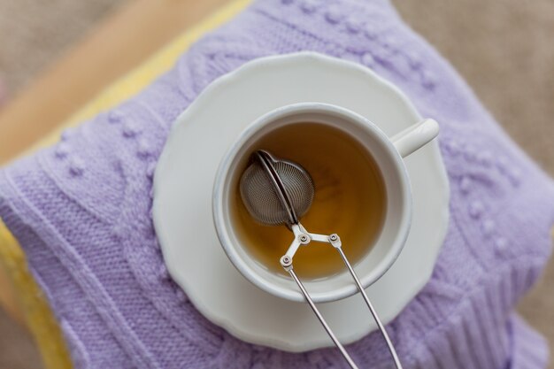 Uma pilha de roupas de malha em uma cadeira de madeira, uma caneca de chá quente