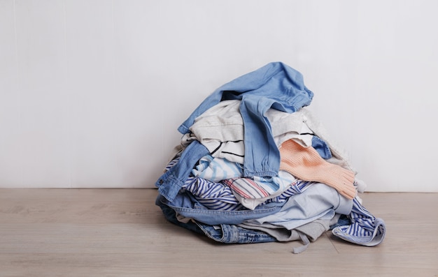 Uma pilha de roupas multicoloridas sujas, preparadas para serem lavadas, está caída no chão ao fundo claro