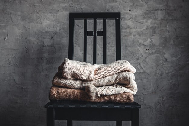 Uma pilha de suéteres aconchegantes de tricô em uma cadeira perto da parede cinza