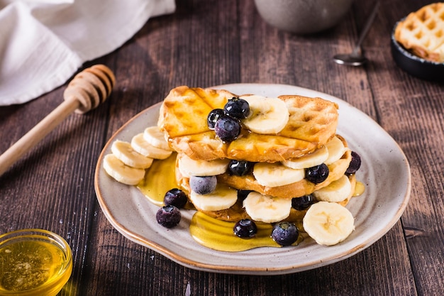 Uma pilha de waffles com mirtilos de banana e mel em um prato Comida reconfortante