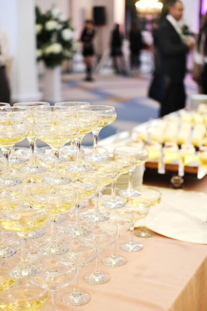 Uma pirâmide de taças de champanhe em uma festa tendo como pano de fundo um salão com convidados pirâmide de champanhe