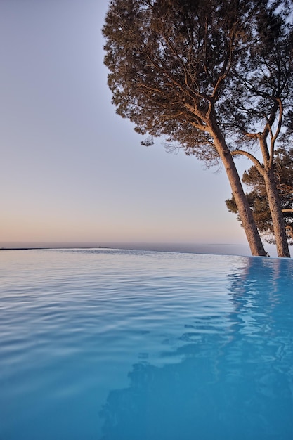 Uma piscina de borda infinita com árvores contra um fundo de céu azul com copyspace Linda piscina ao ar livre em um resort ou vivenda de férias de luxo contra uma escapadela romântica com vista para o mar no verão