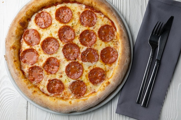 Uma pizza com calabresa está sobre uma mesa ao lado de um garfo e guardanapo.