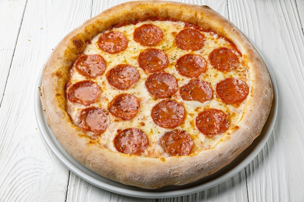 Uma pizza com calabresa sobre uma mesa de madeira branca.
