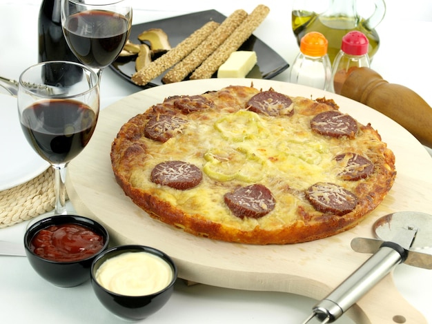 Uma pizza com linguiça ao lado de duas taças de vinho.