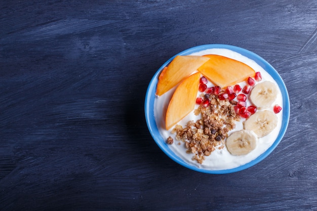 Uma placa azul com iogurte grego, granola, caqui, banana, romã no preto.