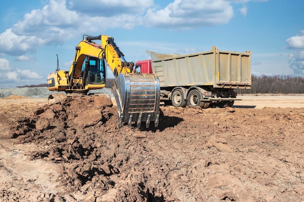 Uma poderosa escavadeira de esteira carrega a terra em um caminhão basculante contra o céu azul Desenvolvimento e remoção do solo do canteiro de obras