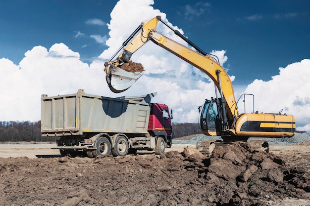 Uma poderosa escavadeira de esteira carrega a terra em um caminhão basculante contra o céu azul Desenvolvimento e remoção do solo do canteiro de obras