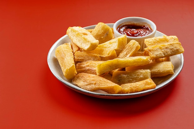 Uma porção de mandiocas fritas em uma comida tradicional brasileira de fundo vermelho