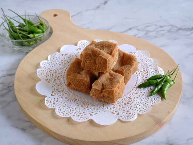 Uma porção de Tofu frito servido com pimentas de caiena em bandeja de madeira com fundo de mármore branco