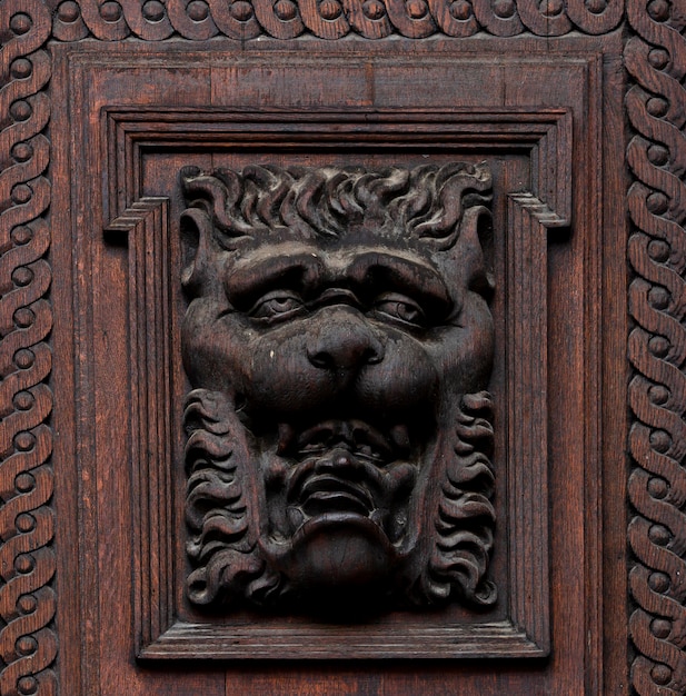 Uma porta de madeira esculpida tem uma face e uma moldura ao redor.