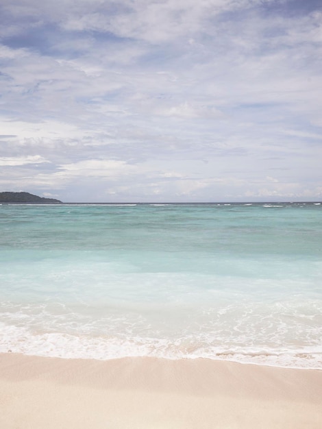 Foto uma praia com água azul e uma pessoa parada nela