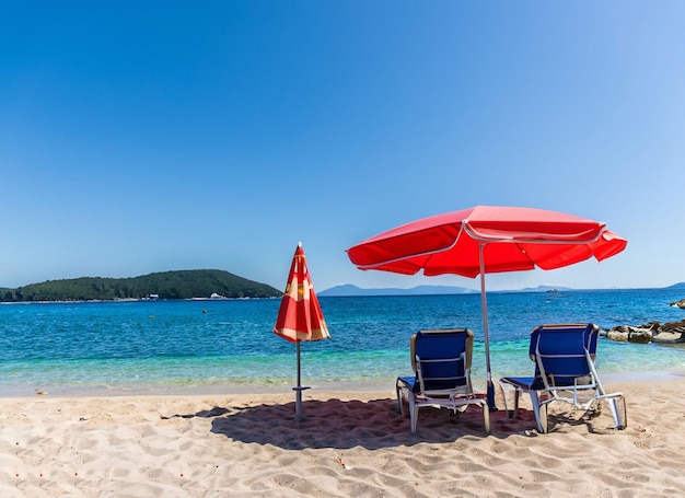 Uma praia com um guarda-chuva vermelho e duas cadeiras de praia na areia.