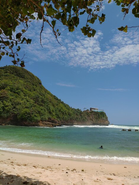 Foto uma praia com um morro ao fundo e uma casa à direita.